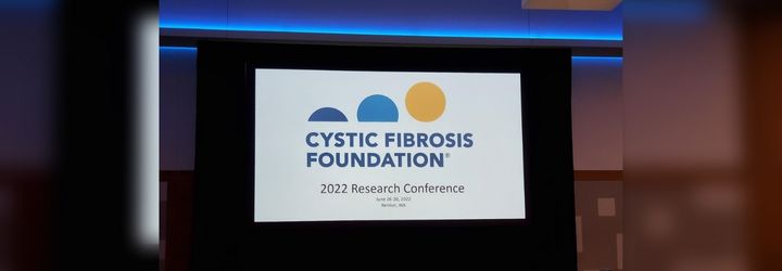 The opening slide on a projector in a conference room reading: Cystic Fibrosis Foundation 2022 Research Conference 