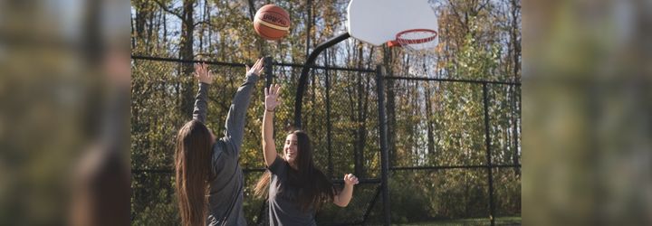 Two girls playing basketball at an outdoor court surrounded by trees.