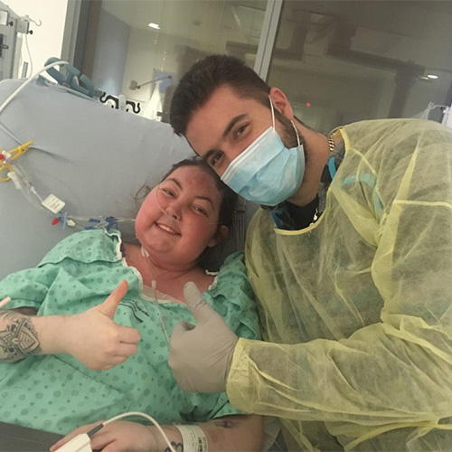 Sandra and her husband holding their thumbs up in a hospital room.