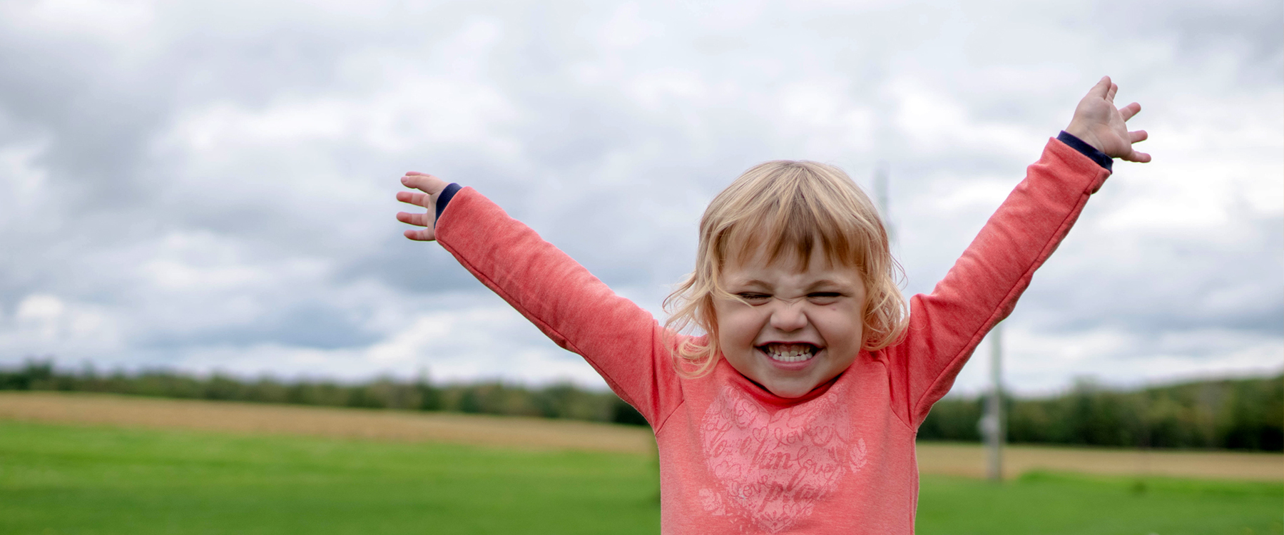 A little girl smiling wide with arms in the sky. 