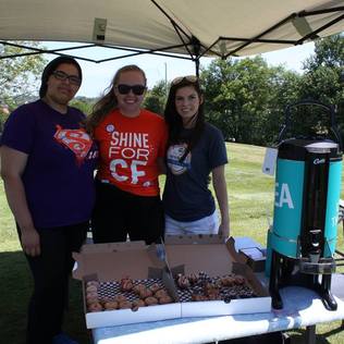 Three women under a canopy behind a half-full box of donuts and a carafe of David's Tea