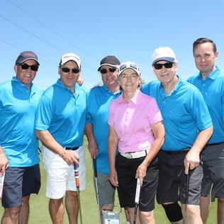Five men in blue golf shirts behind a woman in a pink golf shirt