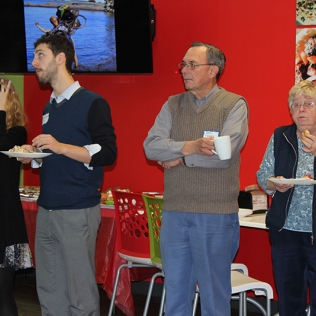 Four people standing, holding plates, and listening