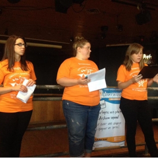 3 women in orange shirts making a presentation