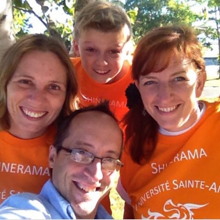 3 people in orange Université de Sainte-Anne shirts with a man