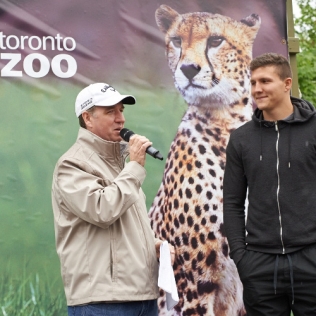 a man with a mike in front of a Toronto Zoo sign