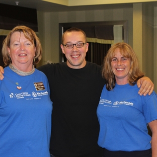 A man with glasses in between two women in blue shirts